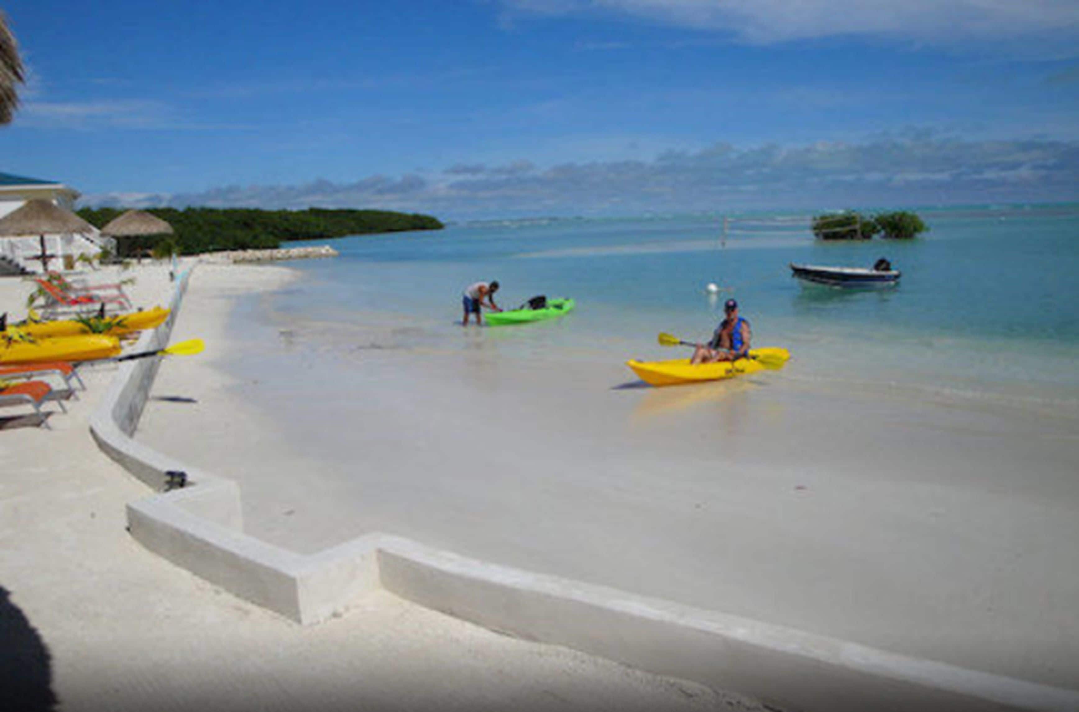A beach with kayaks, a boat, and a thatched-roof structure.