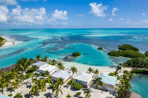 An aerial view of a coastal resort with multiple bungalow-style buildings, clear turquoise waters, and lush greenery. - Shaka Caye - All inclusive (Little Frenchman Caye)
