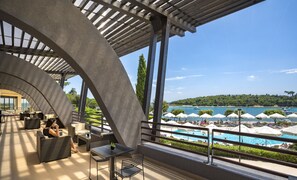 A modern outdoor lounge area with a pool view, featuring a curved ceiling structure, outdoor seating, and a railing overlooking the pool. - Maistra Select All Suite Island Hotel Istra  (Rovinj)
