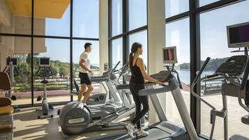 A gym with treadmills, exercise bikes, and a large window offering a view of a body of water and greenery.