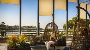 A person sitting in a wicker chair on a rooftop terrace with a view of a bridge and greenery. - Maistra Select All Suite Island Hotel Istra  (Rovinj)