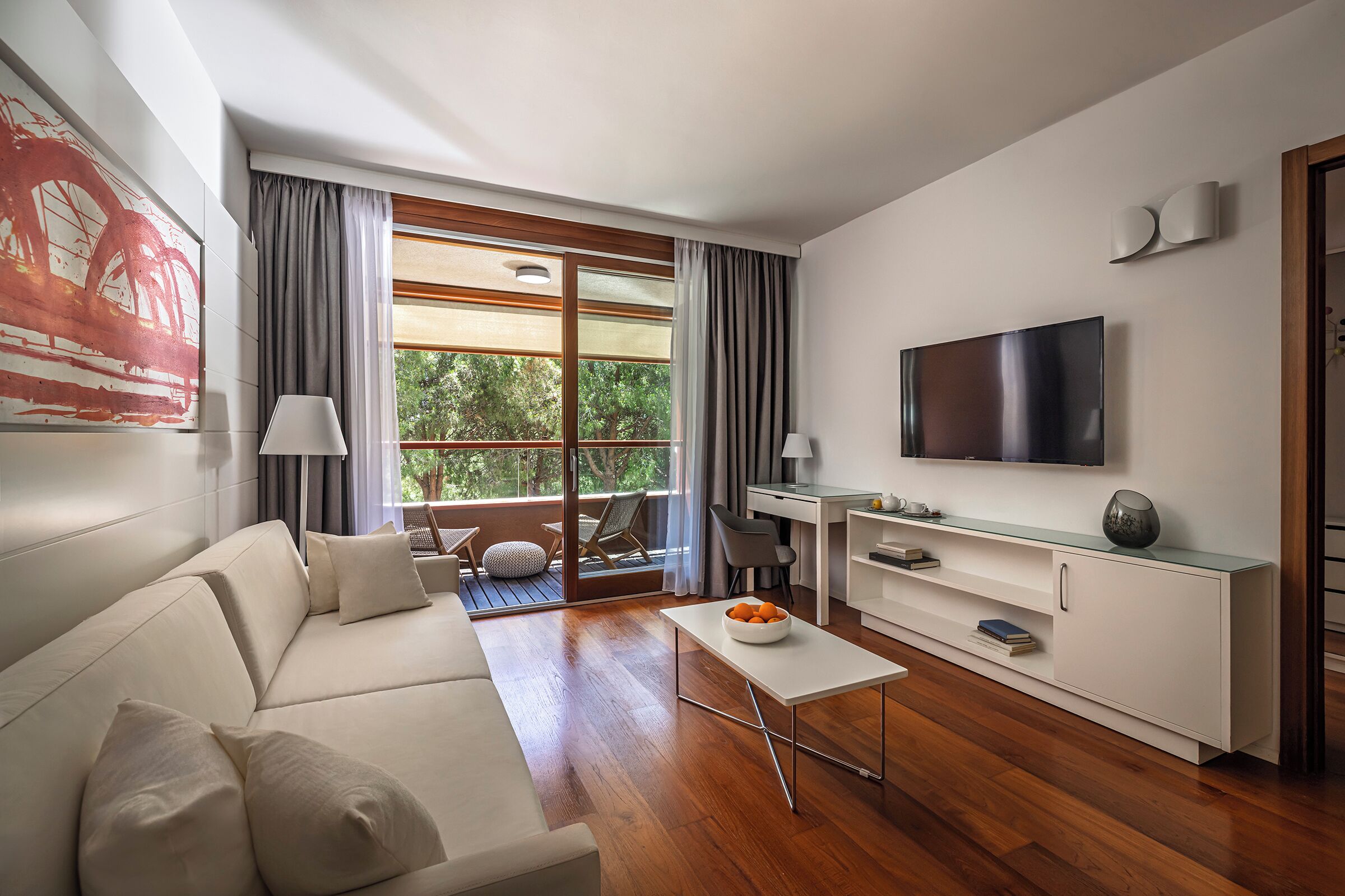 A modern living room with a sofa, coffee table, TV, and a balcony with a view.