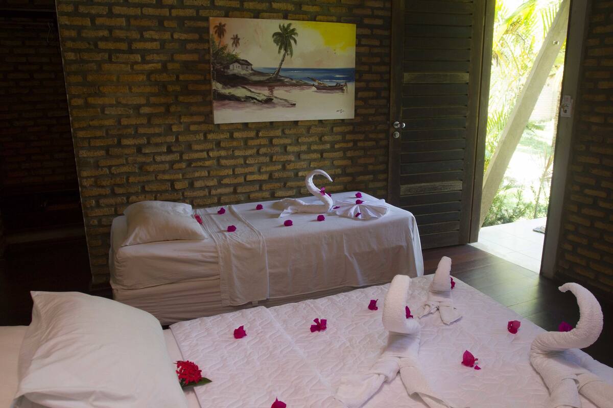 A room with two beds, a brick wall, a painting of a beach, and a door leading outside.