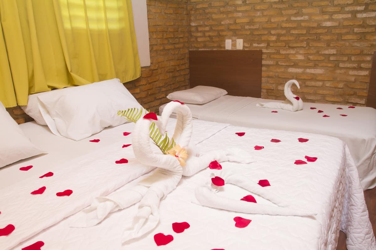 A hotel room with two beds, a brick wall, and a yellow curtain.