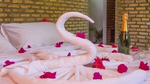 Cama com toalha em formato de cisne, pétalas de rosa e uma garrafa de champanhe.