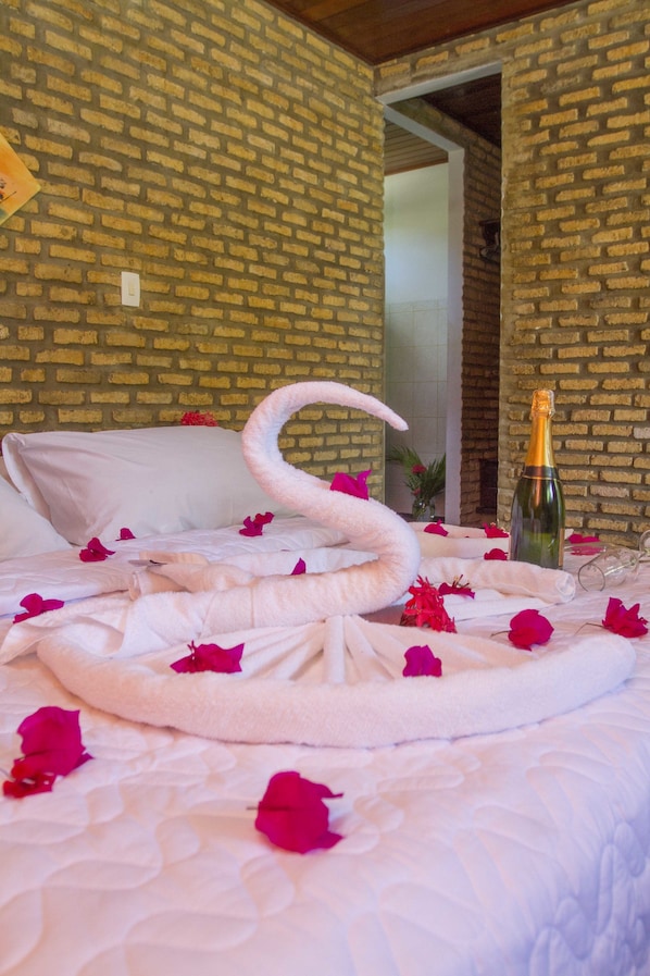 Una cama con una toalla con forma de cisne, pétalos de rosa y una botella de champán.