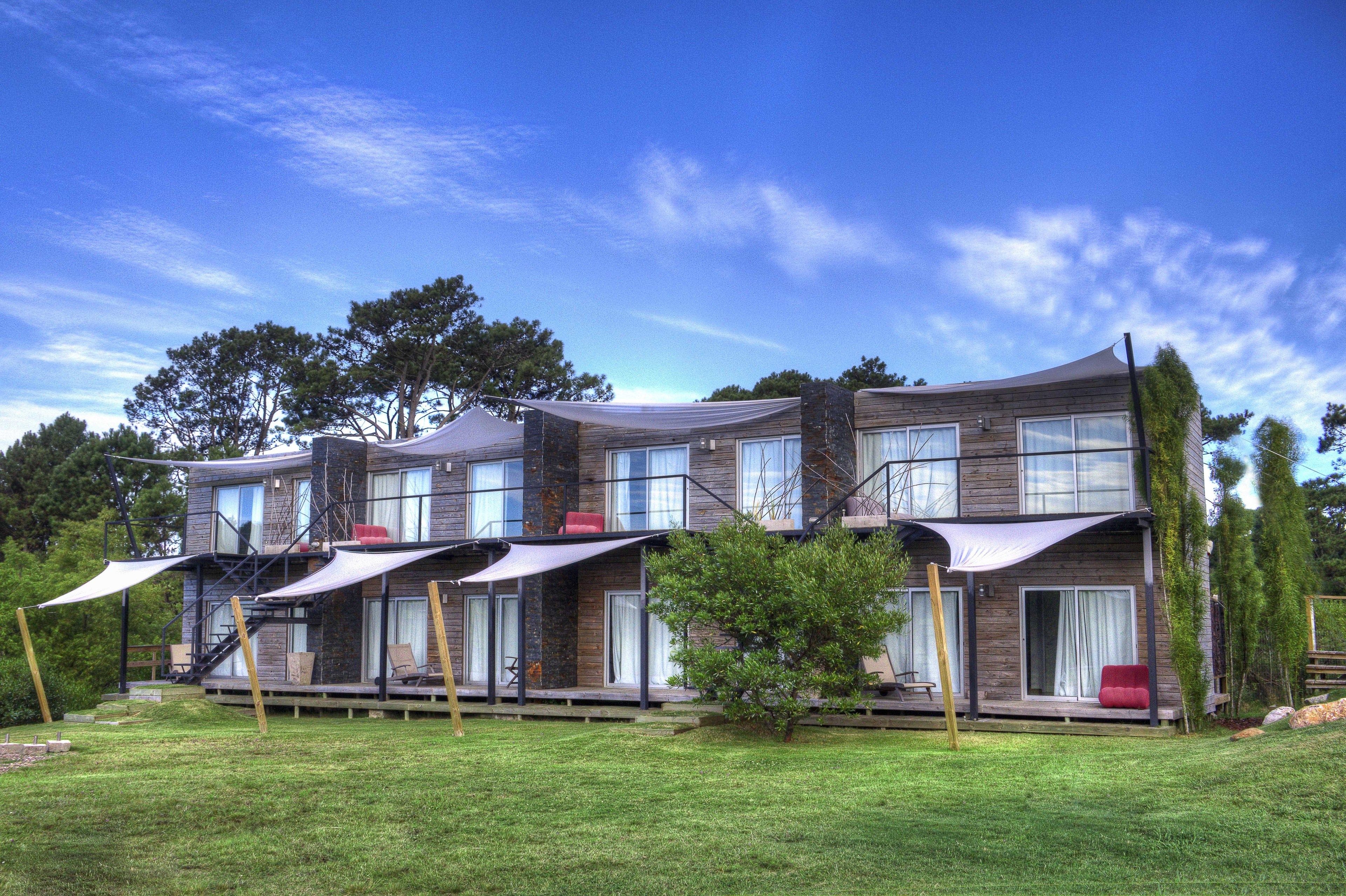 Une maison moderne à deux étages, avec une façade en bois, de nombreux balcons et une pelouse bien entretenue.