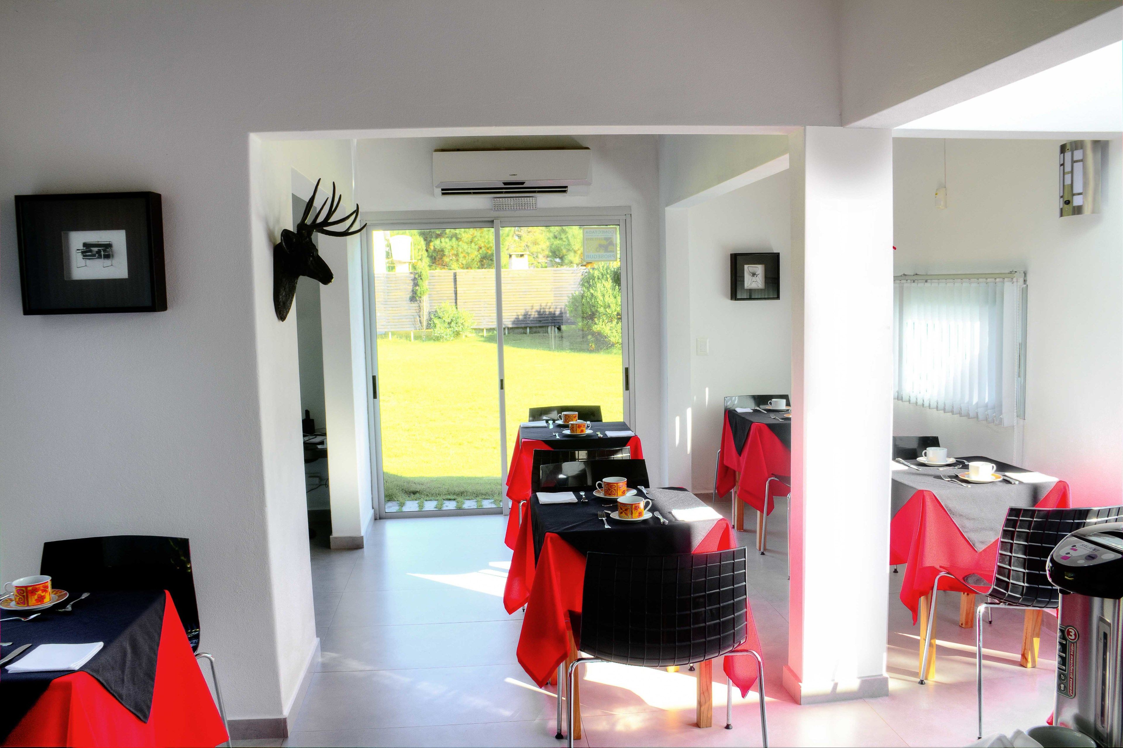 A dining area with tables set for two, red tablecloths, and a mounted deer head on the wall.