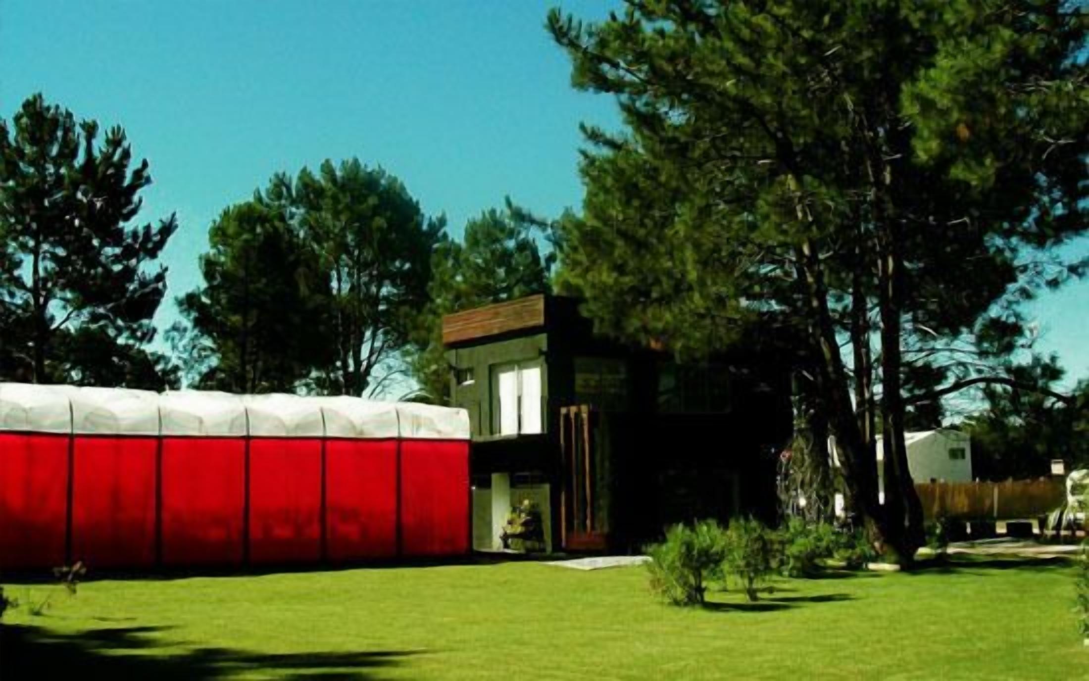 Una casa moderna amb façana vermella i blanca, envoltada d'un jardí ben cuidat i arbres alts.