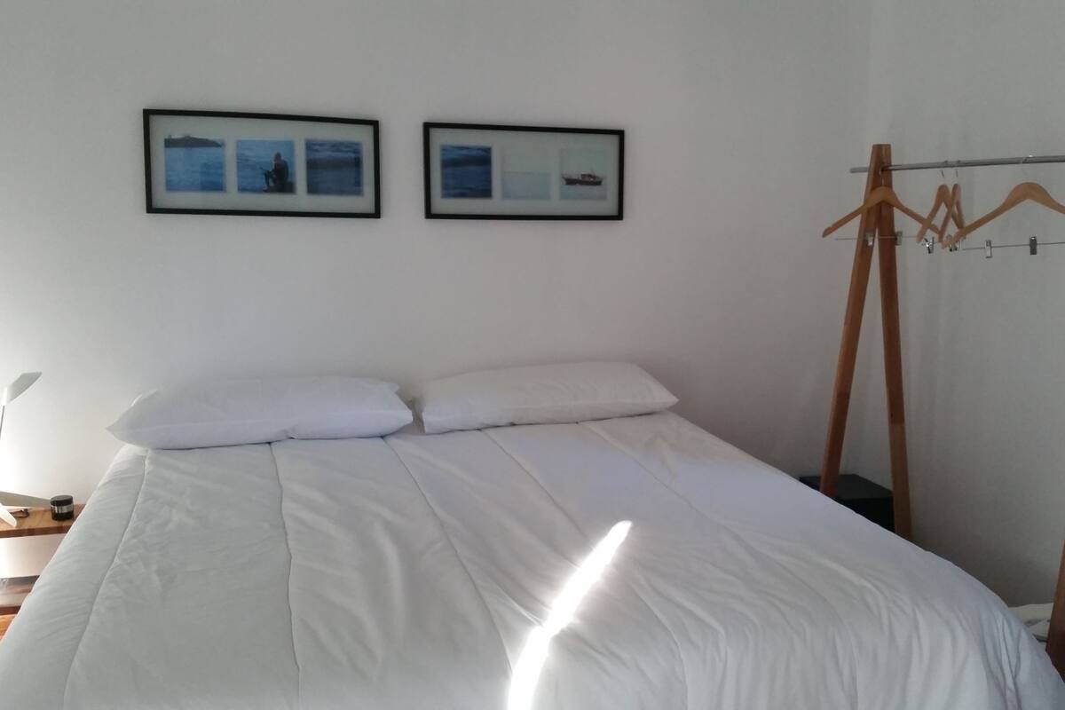 A bedroom with a bed, two framed pictures on the wall, and a wooden drying rack.