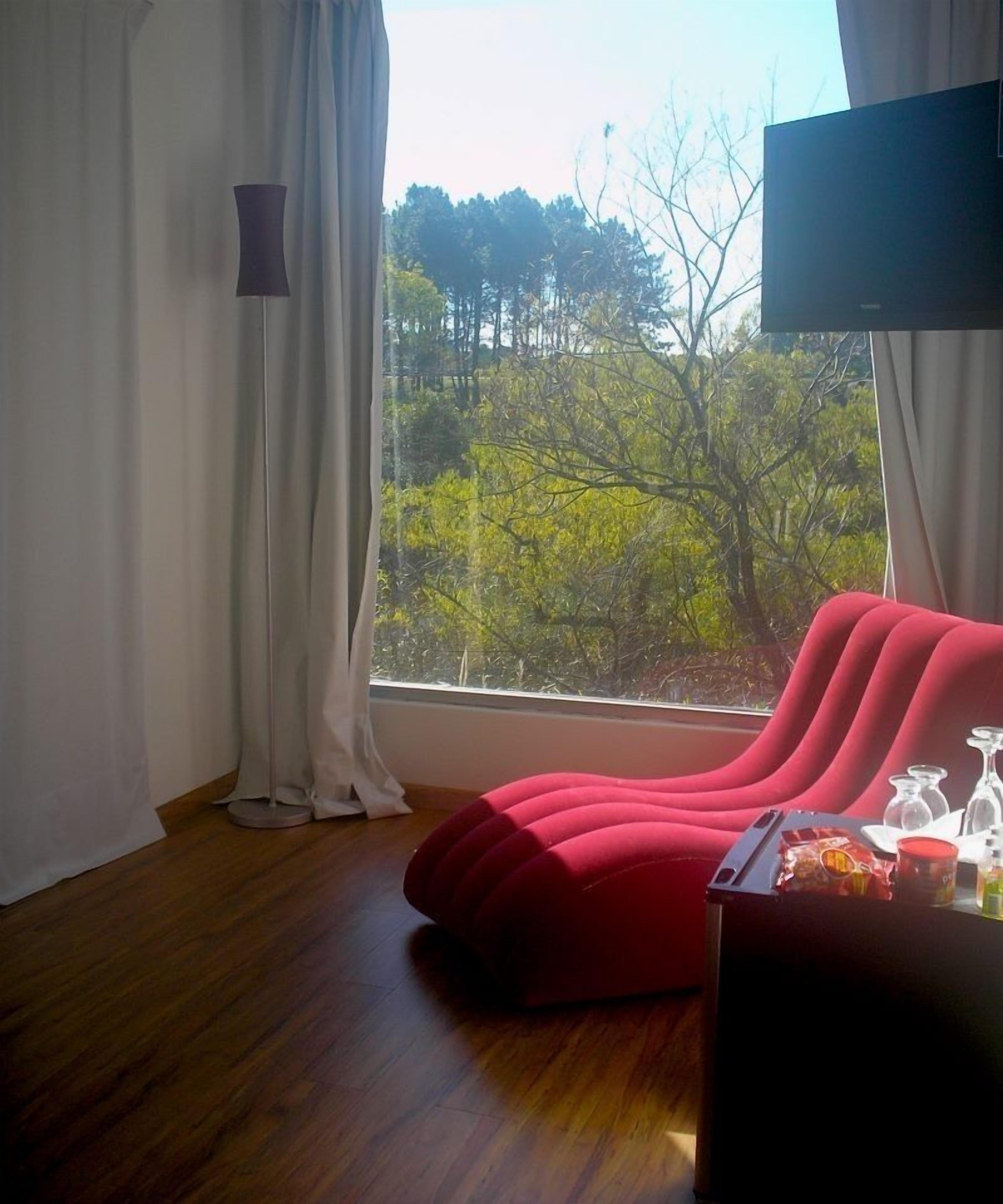 A modern room with a red sofa, a TV, and a view of trees through a window.