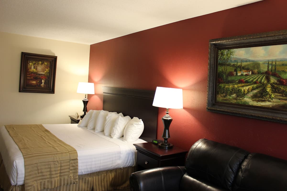 A hotel room with a bed, two bedside tables with lamps, a chair, and a painting on the wall.
