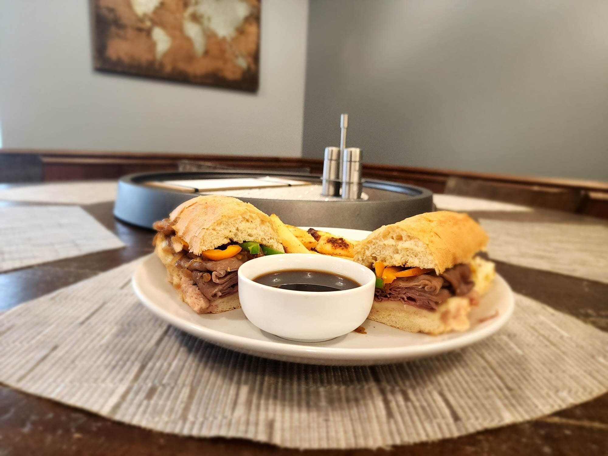A plate with a sandwich and a small cup of sauce on a placemat.