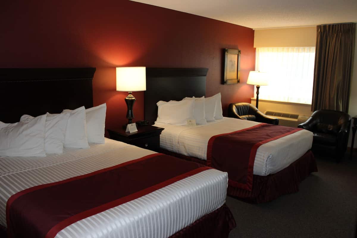 A hotel room with two beds, a desk, a chair, and a window with curtains.