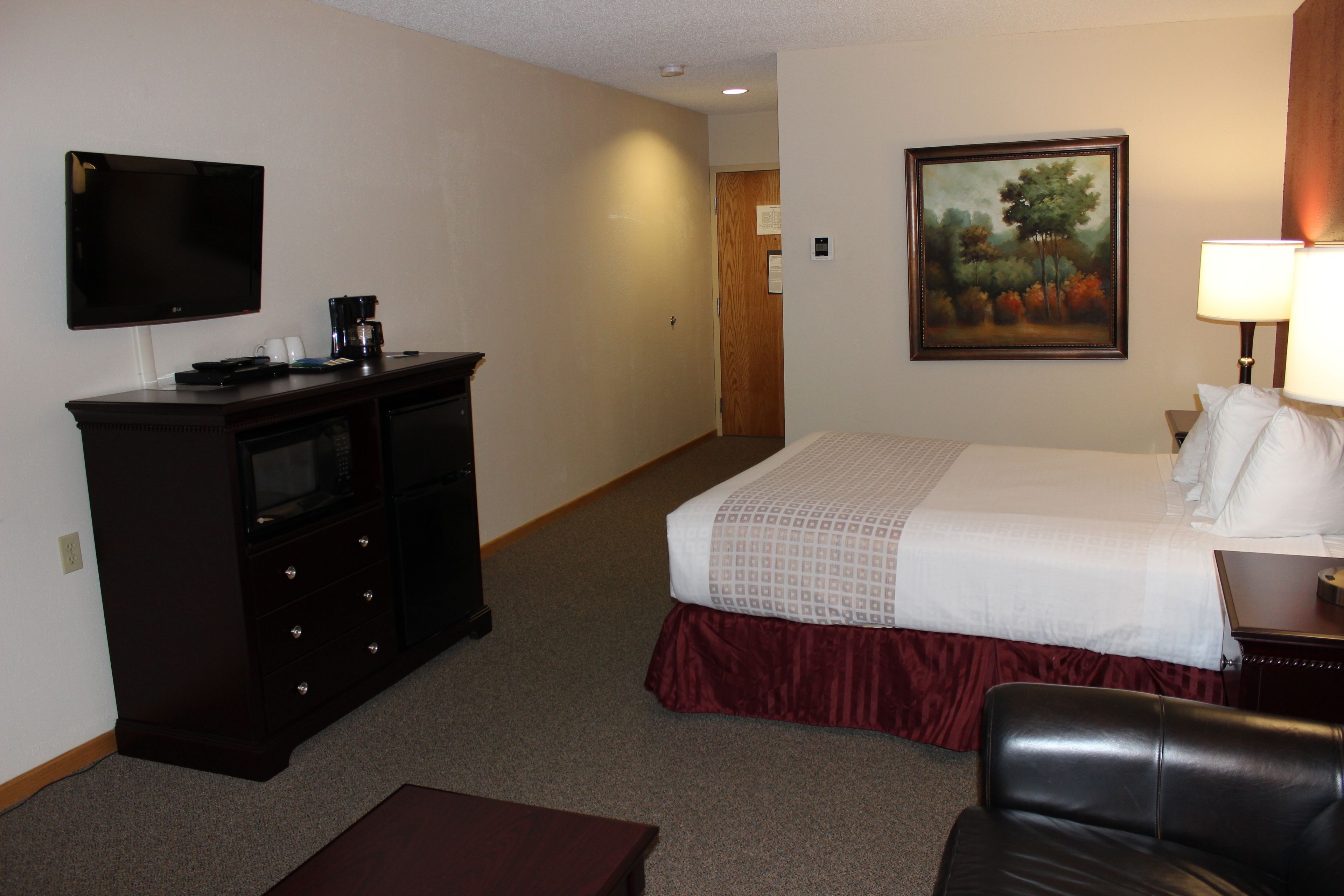 A hotel room with a bed, a television, a desk, and a painting on the wall.