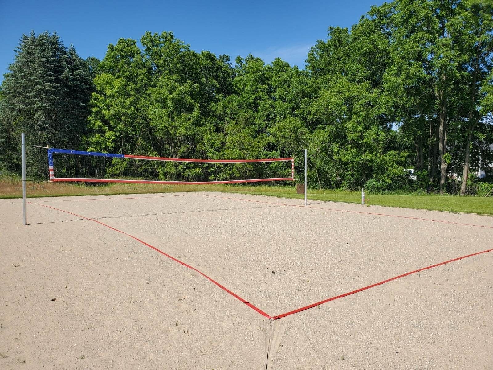 An outdoor volleyball court with a net, surrounded by trees.