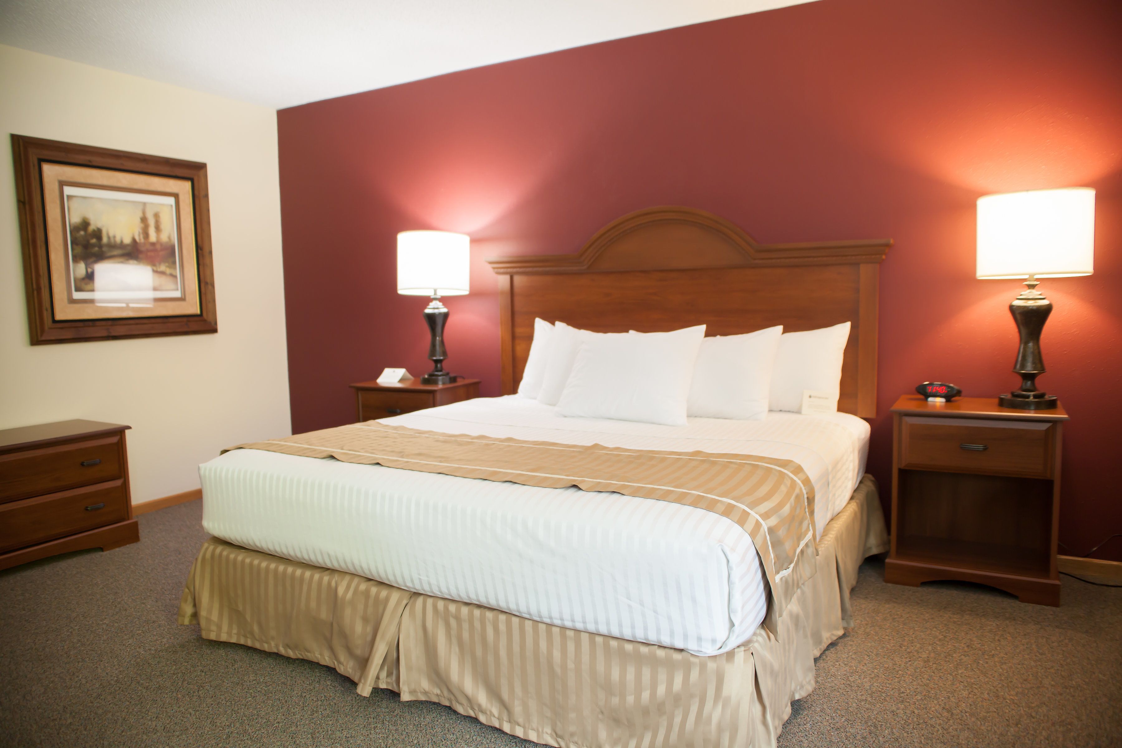 A hotel room with a large bed, two bedside tables with lamps, a wooden headboard, and a framed picture on the wall.