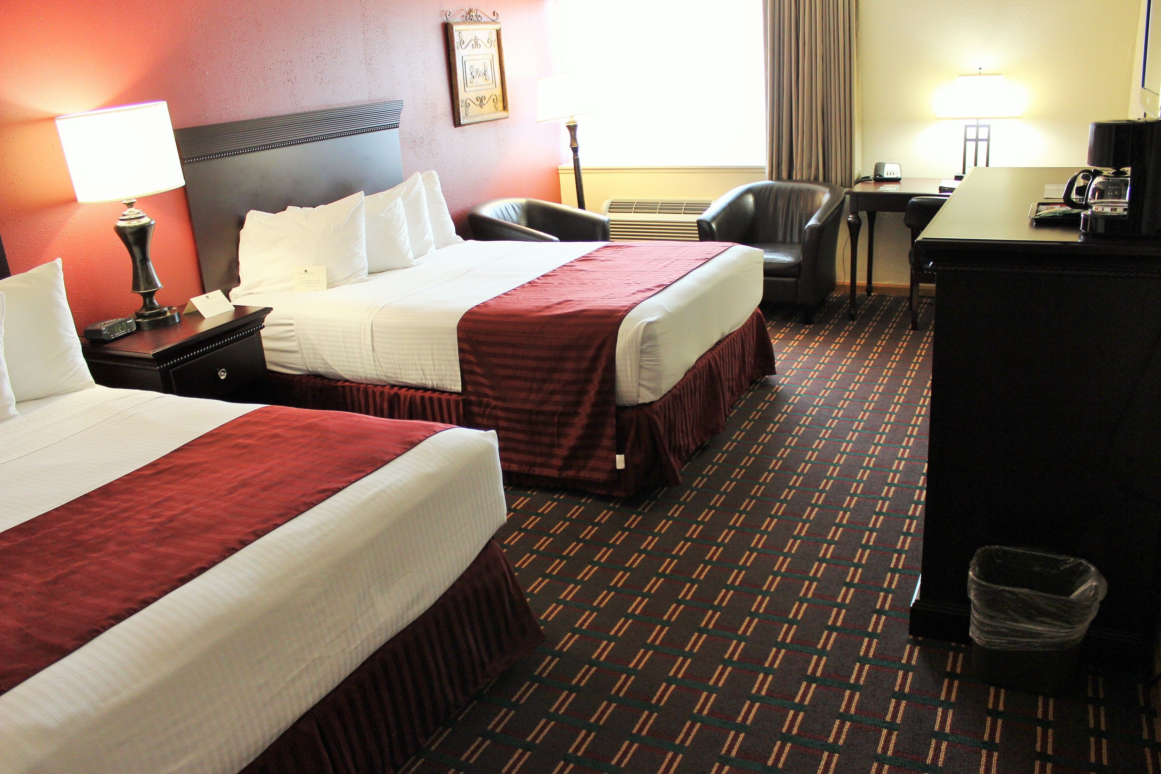 Une chambre d’hôtel avec deux lits, un bureau, une chaise, une poubelle et une lampe.