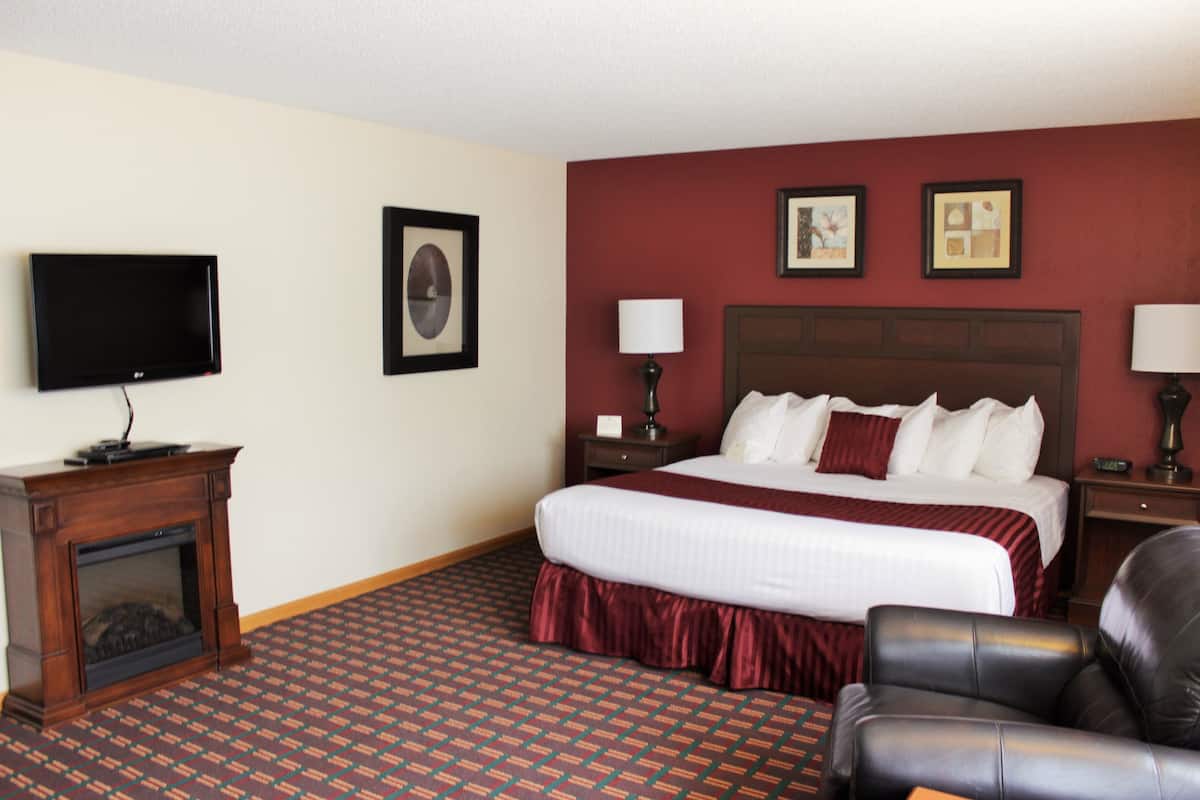A hotel room with a large bed, a flat-screen TV, a fireplace, a desk, and a chair.
