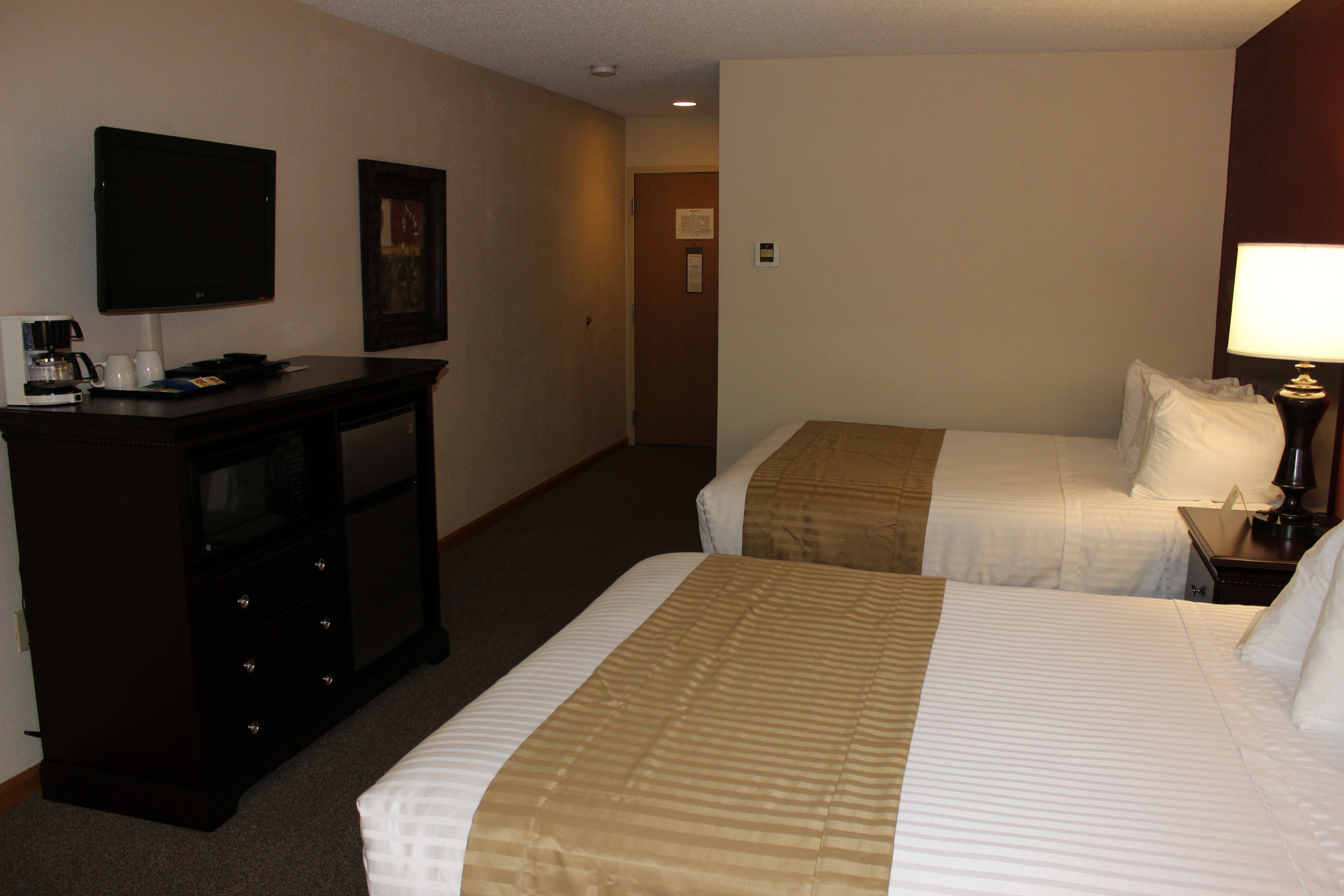 A hotel room with two beds, a desk with a coffee maker, a TV, and a lamp.