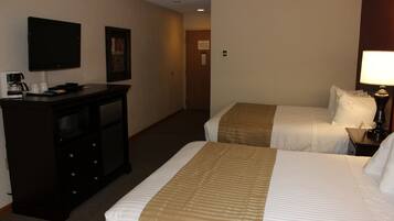 A hotel room with two beds, a desk with a coffee maker, a TV, and a lamp.