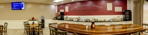 A hotel lobby with a large curved wall displaying "Welcome to Fremont, Michigan" and a digital screen above it. There are several tables and chairs arranged for dining.