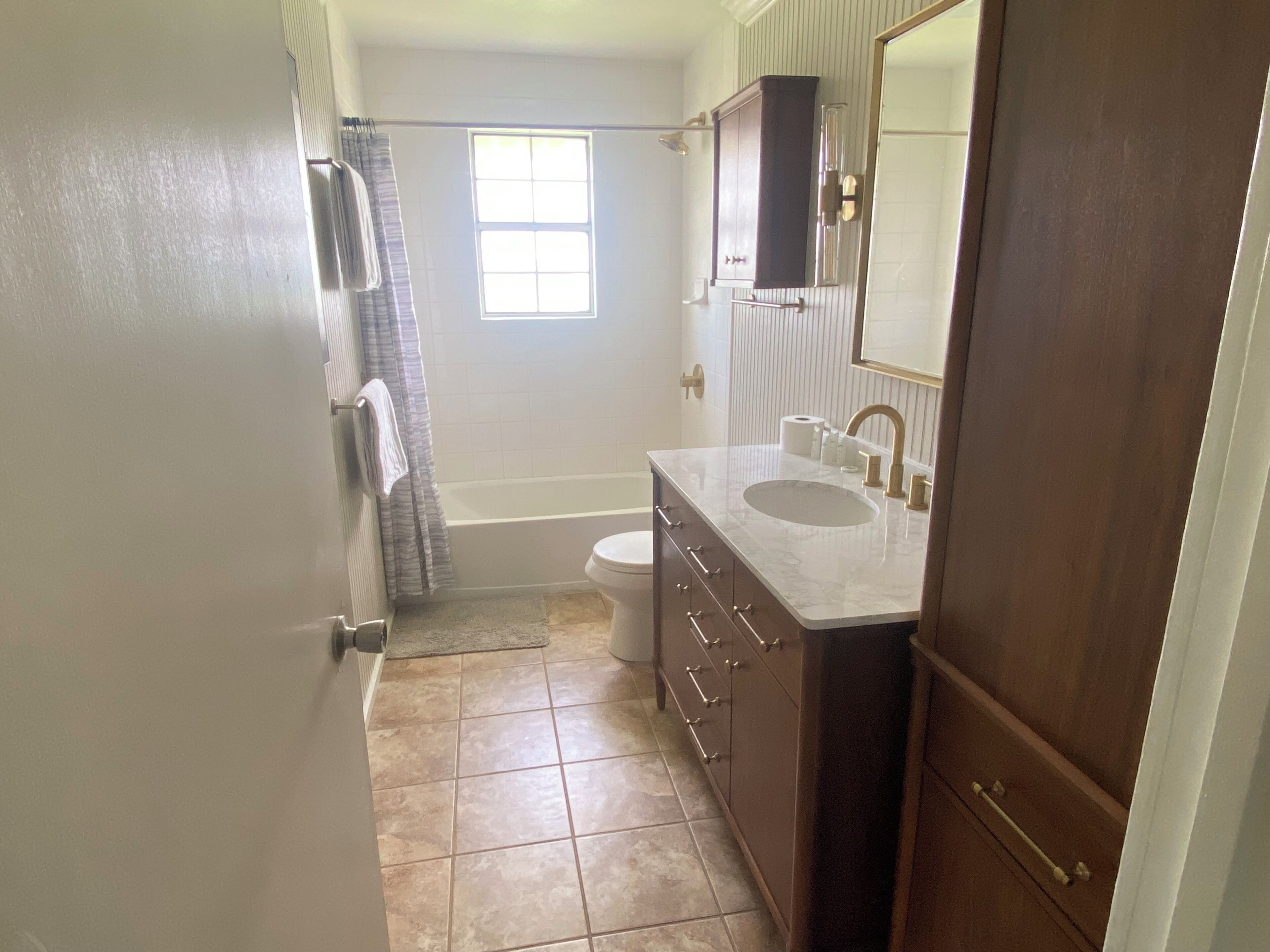 A bathroom with a bathtub, toilet, vanity with a sink, and a window.