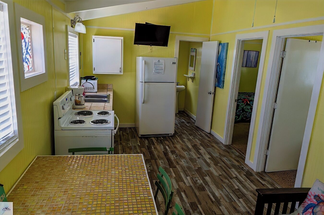 A compact kitchen with a stove, refrigerator, and a television mounted above the fridge.