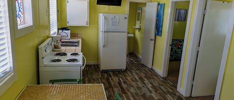 A compact kitchen with a stove, refrigerator, and a television mounted above the fridge.