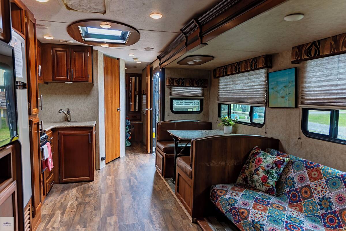 A compact RV interior with a kitchenette, a dining area, and a sleeping space with a colorful quilt.