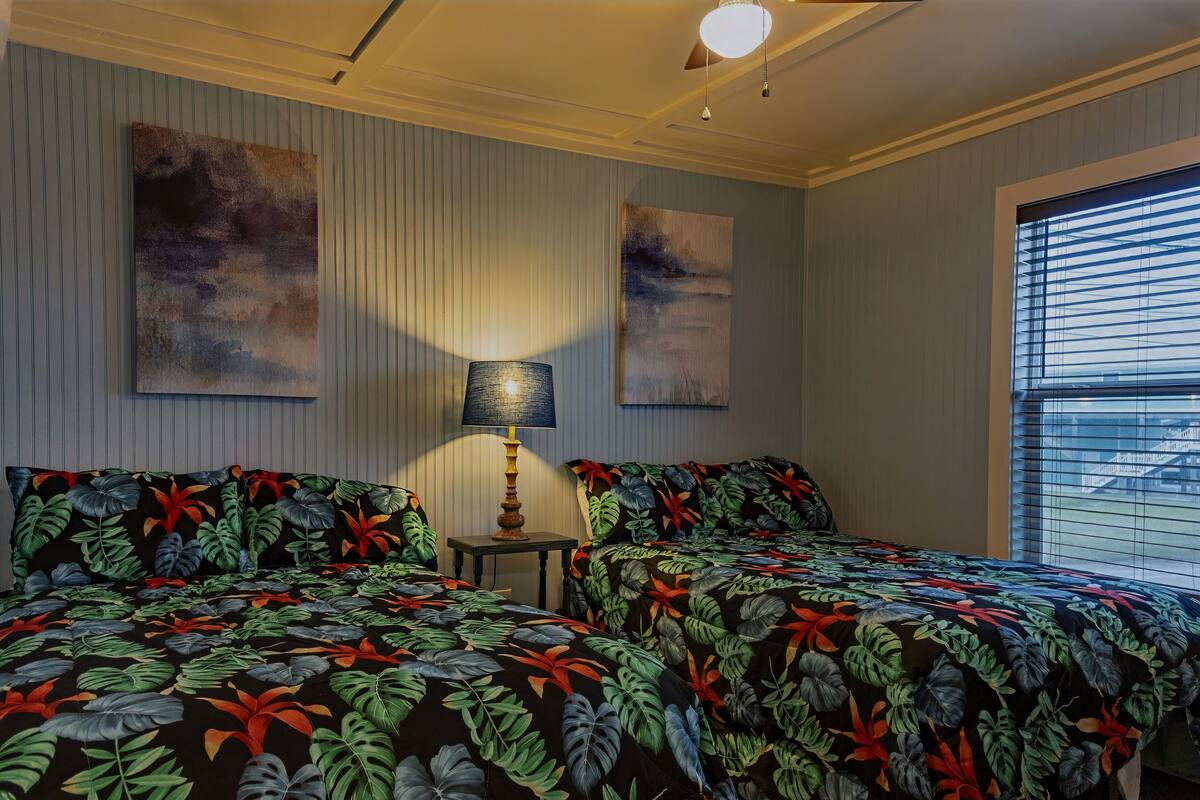 A bedroom with two beds, a nightstand, a lamp, and two wall art pieces.
