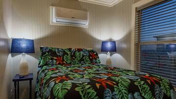 Un dormitorio con cama, dos lámparas de noche, aire acondicionado y una ventana con persianas.