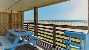 A covered deck with wooden railings overlooking a beach. - Blue Dolphin Inn and Cottages (Grand Isle)