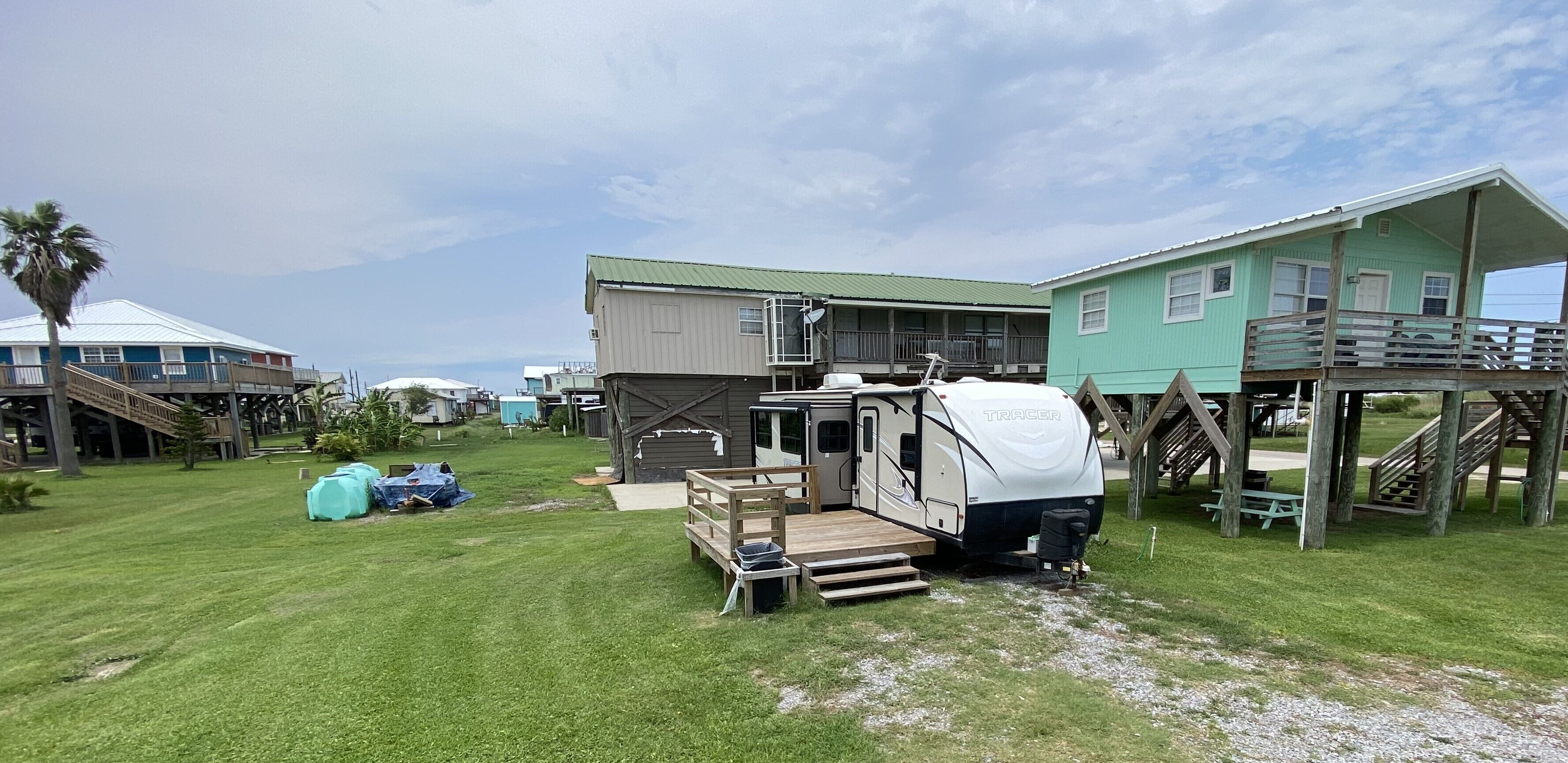 A campsite with a white RV, a green house, and a wooden deck.