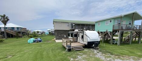 A campsite with a white RV, a green house, and a wooden deck.