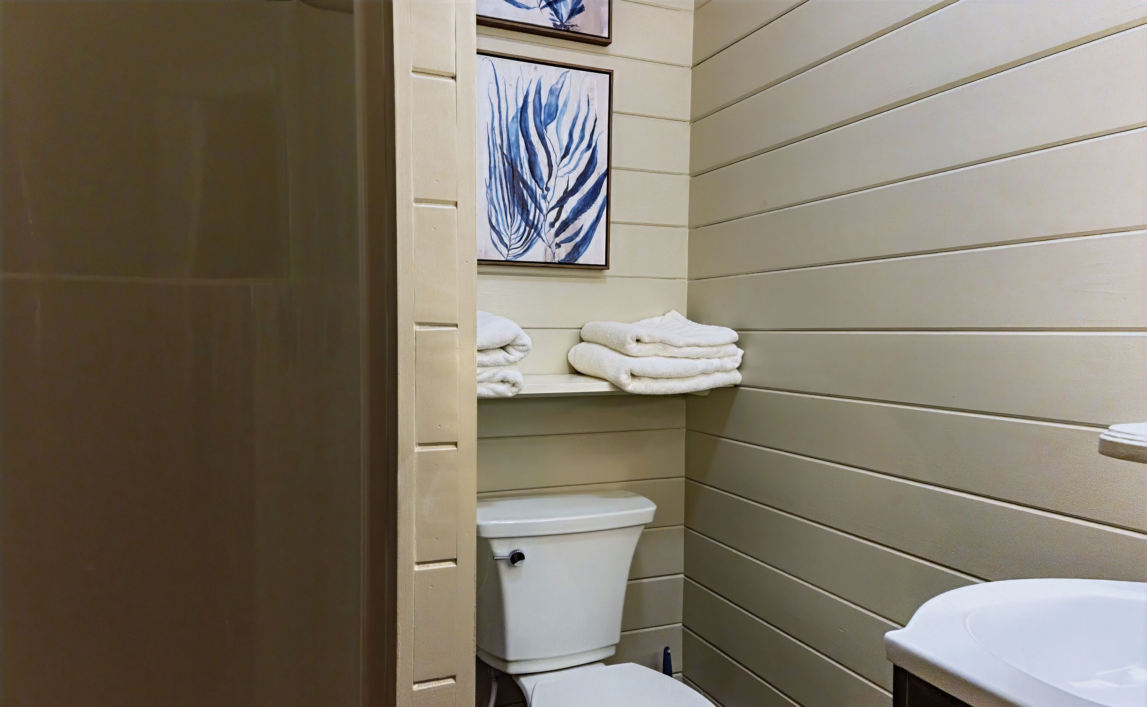 Une salle de bain avec des toilettes, un lavabo et des serviettes rangées sur une étagère.