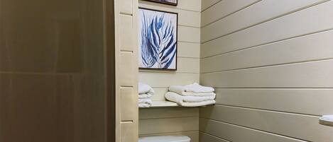 Une salle de bain avec des toilettes, un lavabo et des serviettes rangées sur une étagère.