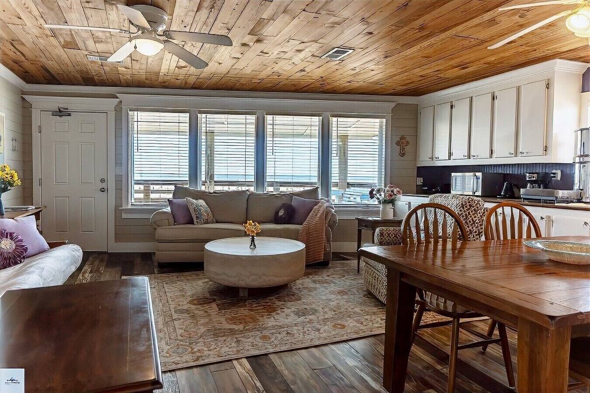 A cozy living room with a wooden ceiling, a sofa, a coffee table, and a dining area with chairs and a table.