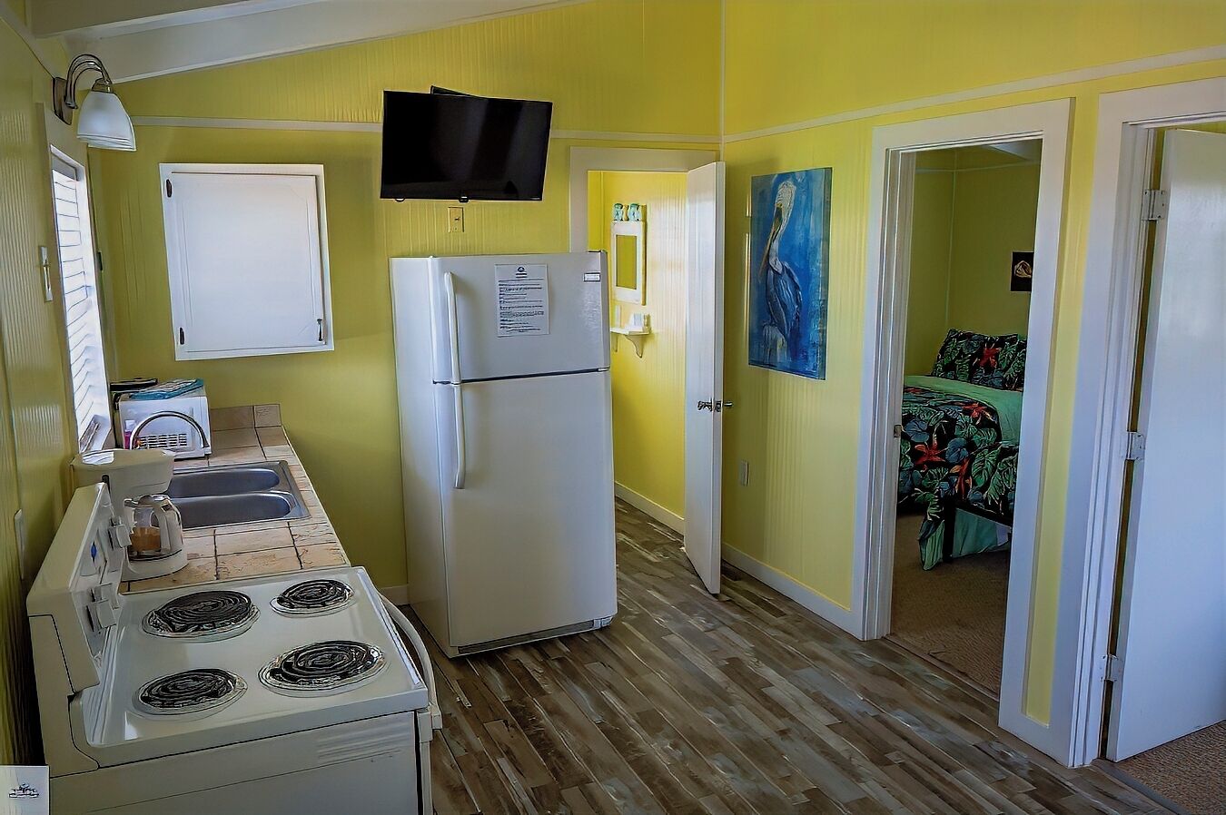 A compact kitchen with a refrigerator, stove, and sink. A television is mounted above the refrigerator.