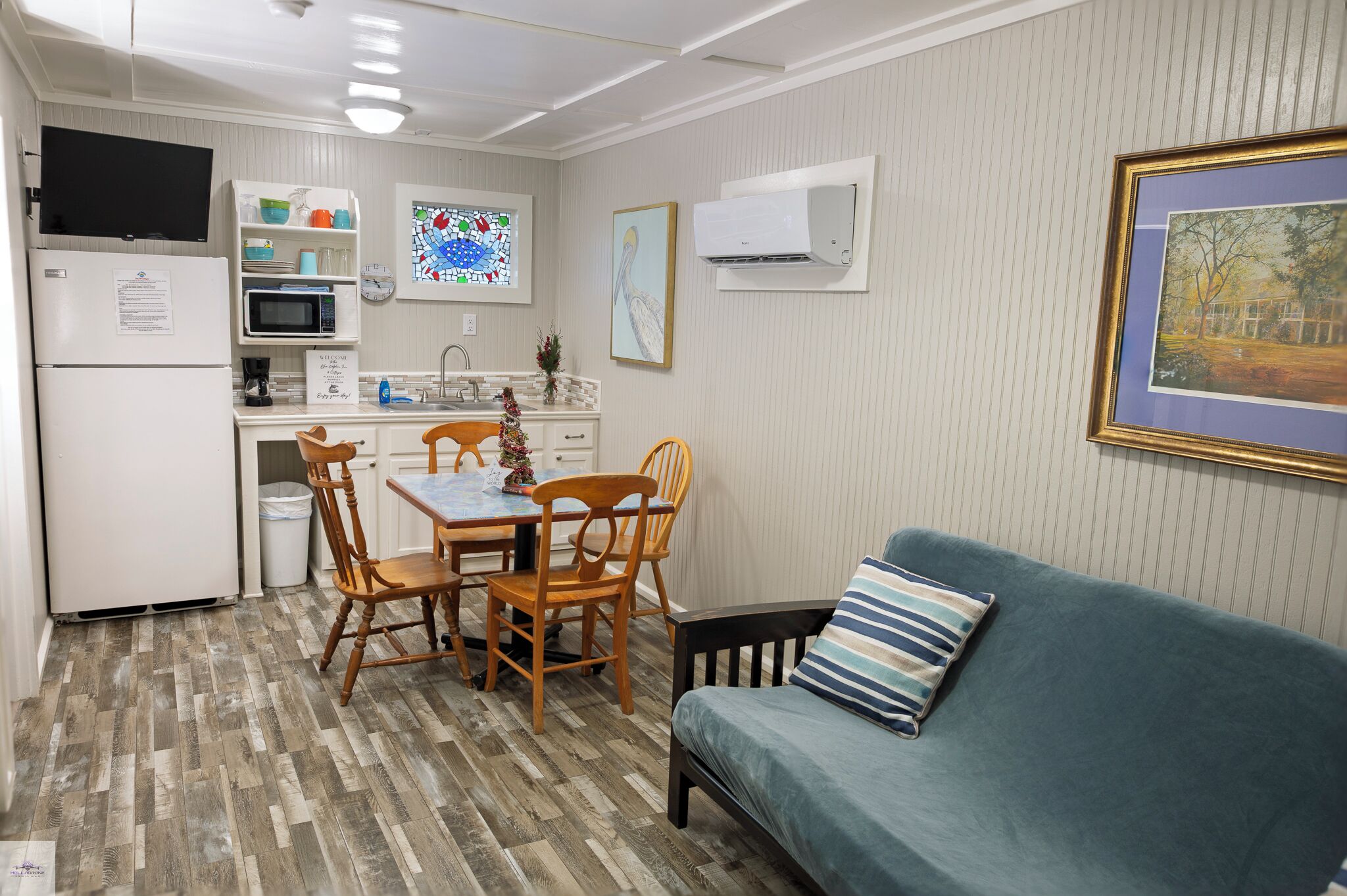 A compact kitchen with a refrigerator, microwave, and sink, a dining table with chairs, and a blue sofa with a striped pillow.