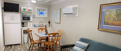 A compact kitchen with a refrigerator, microwave, and sink, a dining table with chairs, and a blue sofa with a striped pillow.