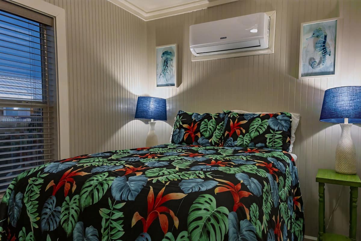 A bedroom with a bed, two wall-mounted lamps, an air conditioner, and a window with blinds.