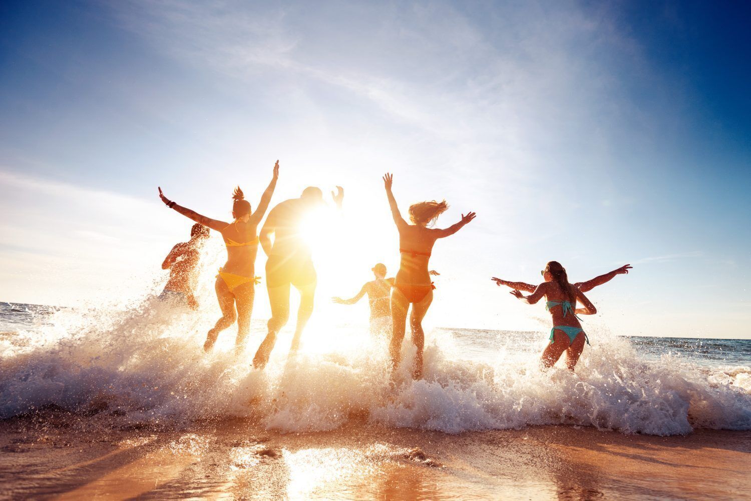 A beach scene with people jumping in the water.