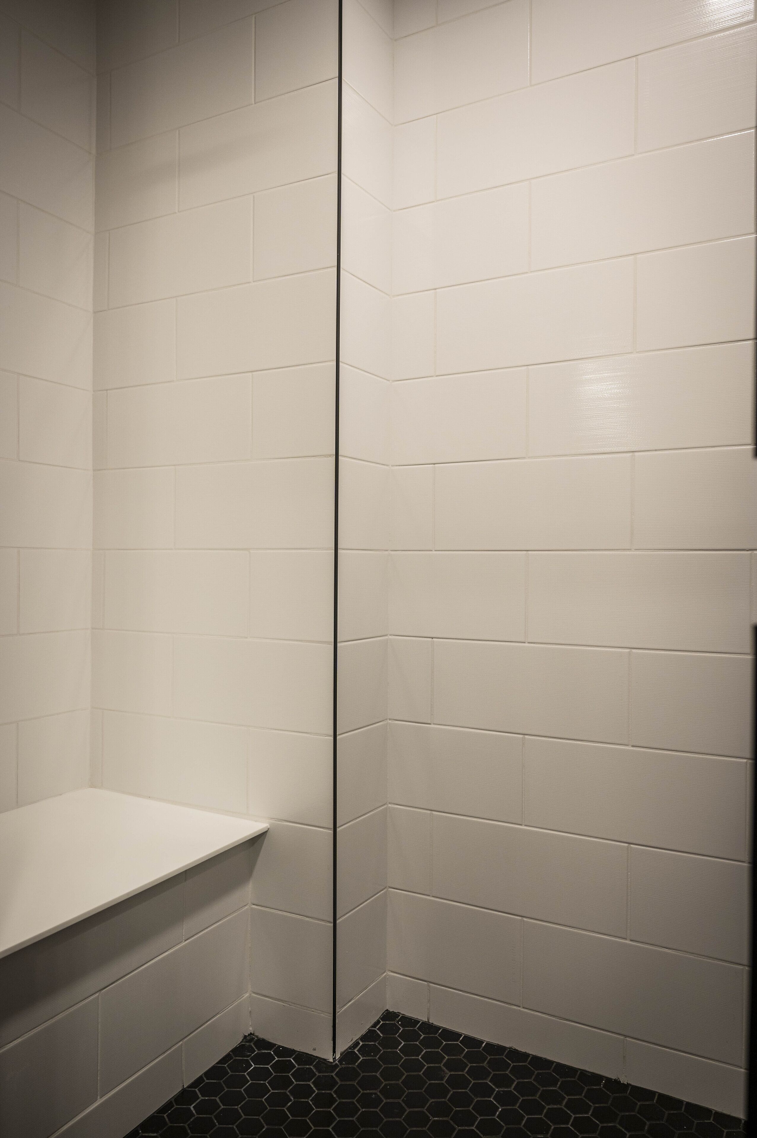 A corner of a bathroom with white tiled walls and a black hexagonal floor.