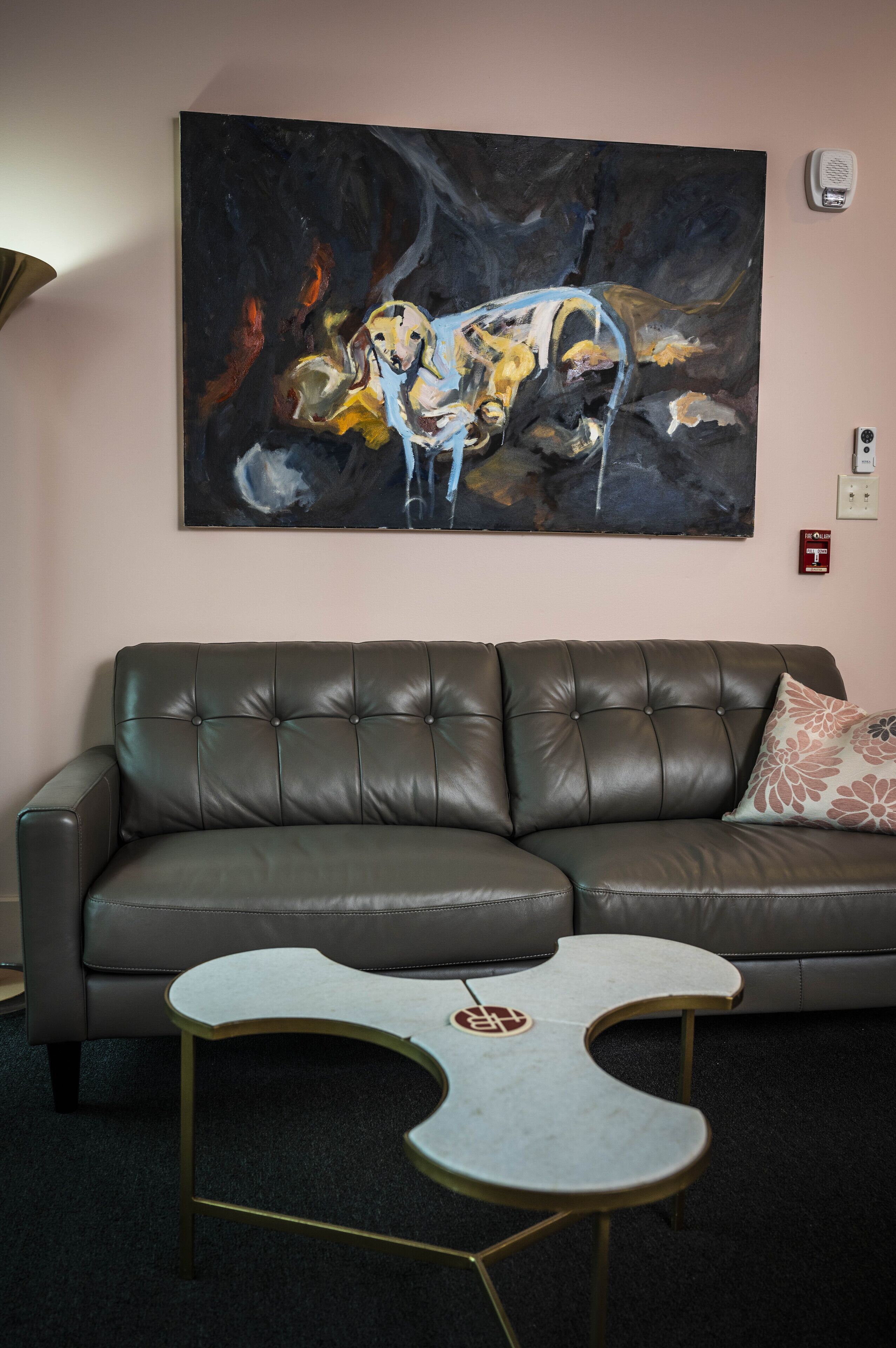 Ein Wohnzimmer mit einem dunkelbraunen Ledersofa, einem einzigartigen weißen Couchtisch und einem großen abstrakten Gemälde an der Wand.
