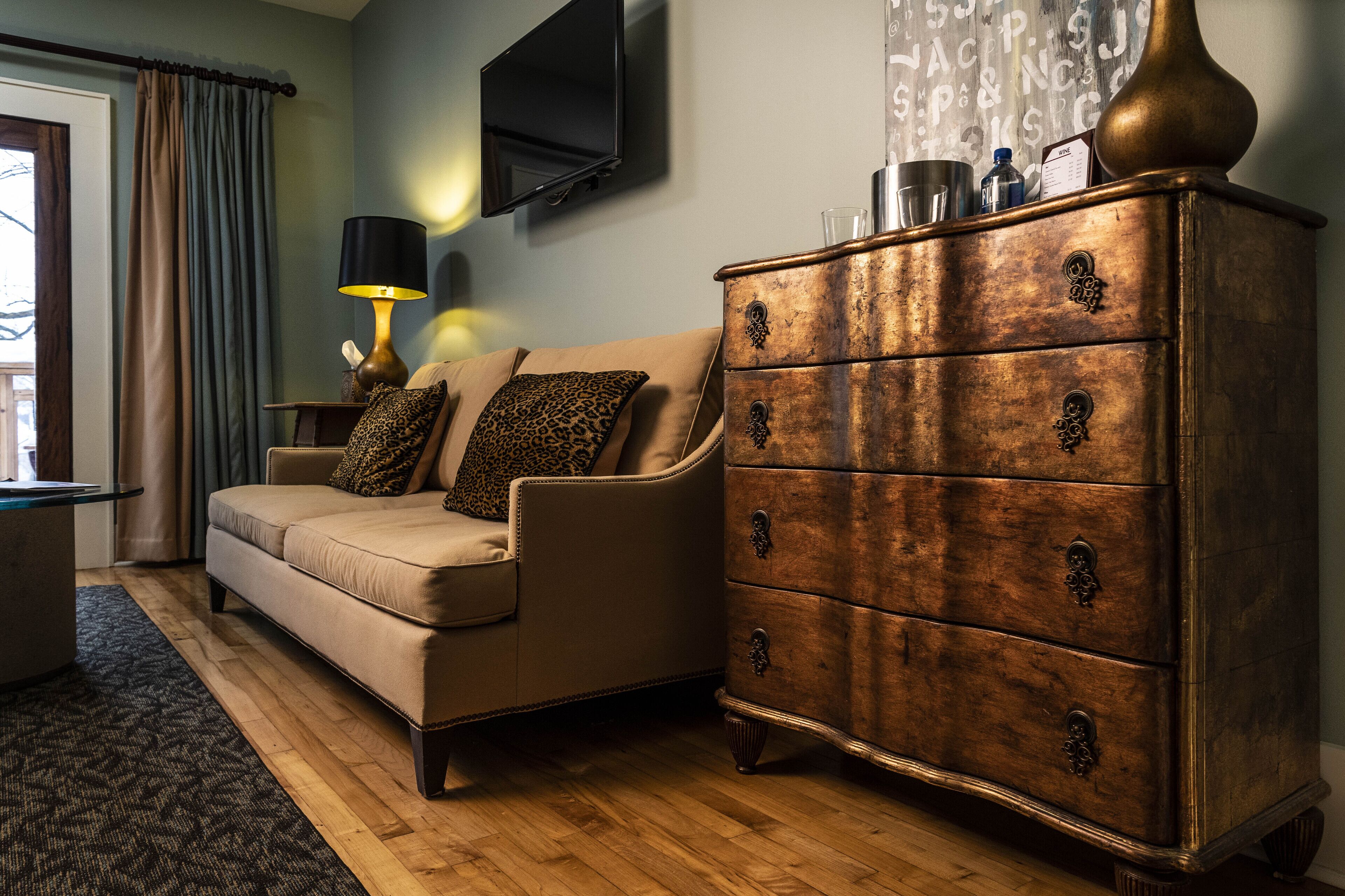A living room with a beige sofa, a wooden dresser with drawers, a lamp, and a flat-screen TV mounted on the wall.