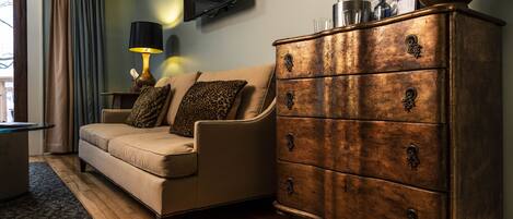 A living room with a beige sofa, a wooden dresser with drawers, a lamp, and a flat-screen TV mounted on the wall.