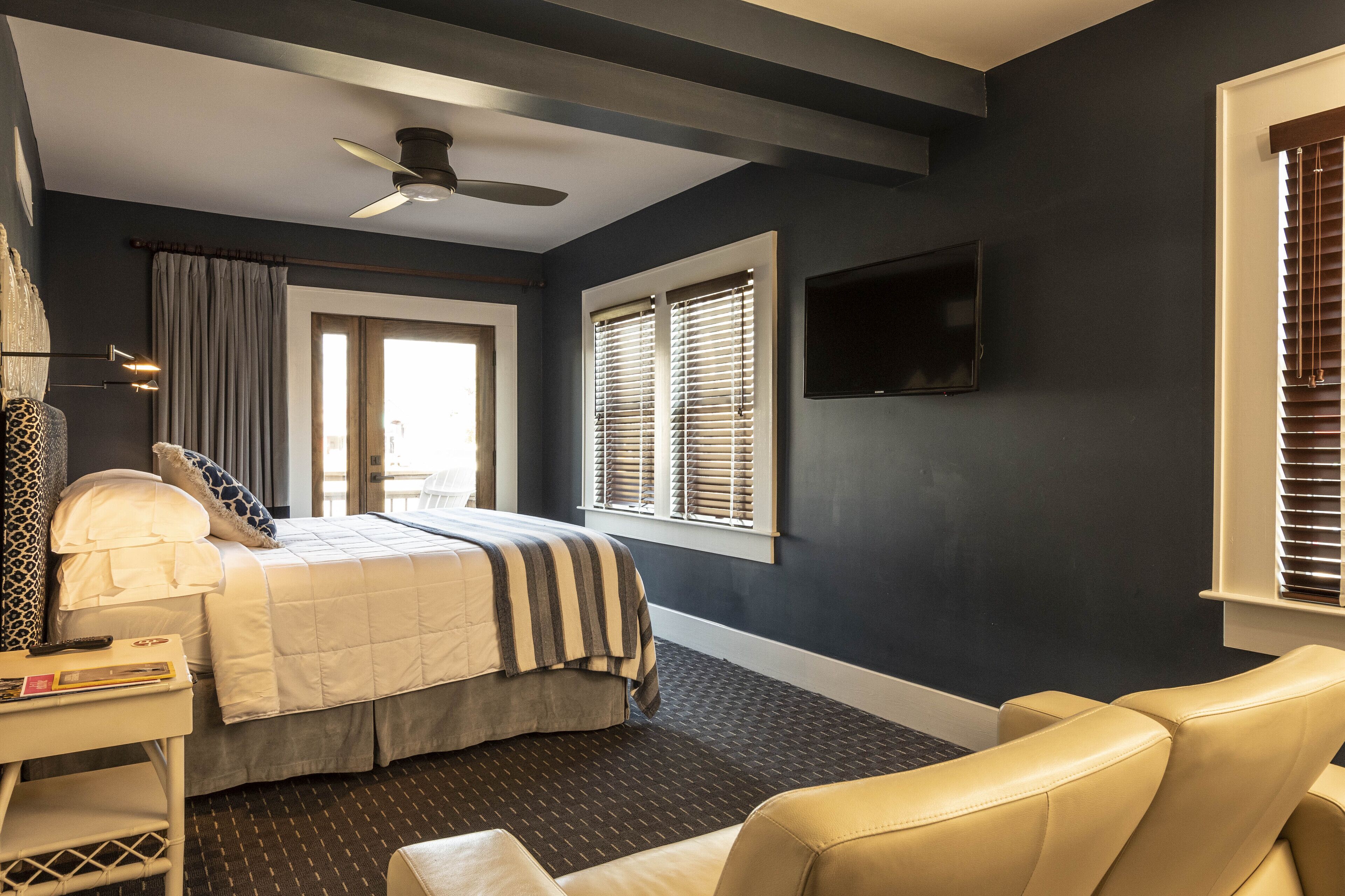 A bedroom with a bed, a desk, a chair, a ceiling fan, and a TV mounted on the wall.