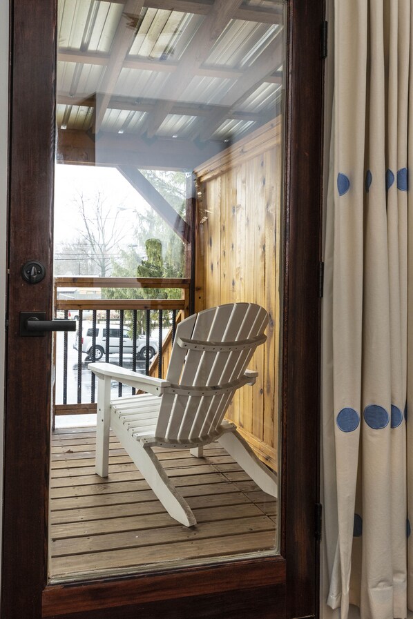 A wooden deck with a white Adirondack chair, a wooden railing, and a view of the street through a glass door.