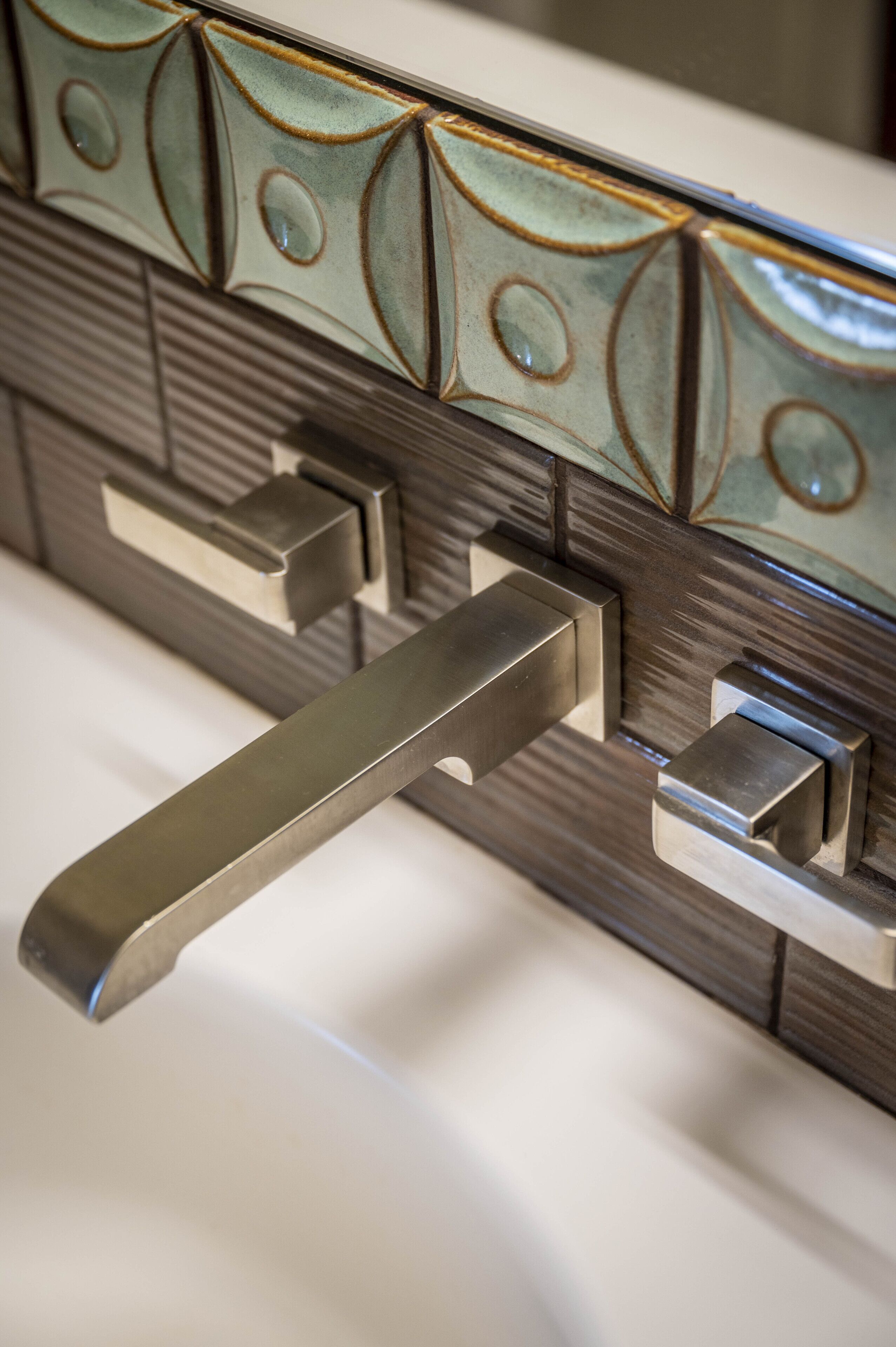 A close-up of a metallic handle attached to a wall with decorative ceramic tiles.